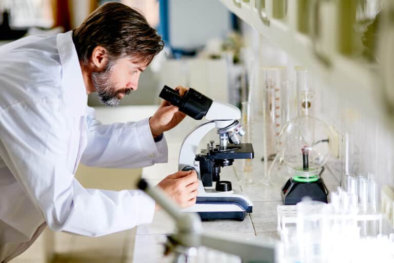 Mature scientist looking in microscope during chemical investigation Quatrefolic® PRO in lab