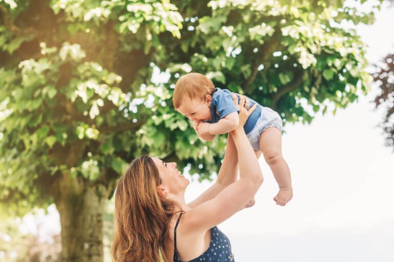 Outdoor portrait of happy mother holding adorable baby boy in air